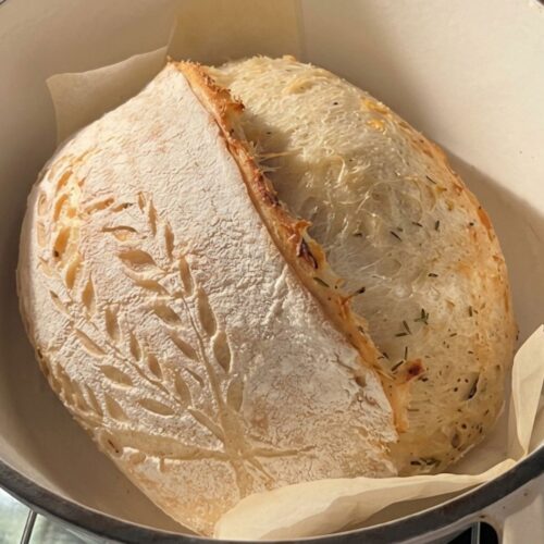 roasted garlic and herb sourdough loaf in a dutch oven pot, herb flecks visible in the crumb