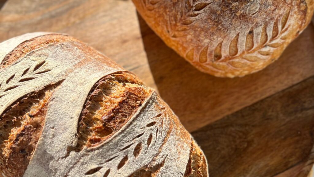 Baked sourdough loaf with a bloomed wheat-stalk scoring pattern across the crust