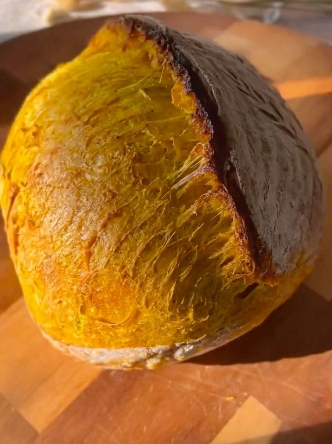 Baked sourdough loaf with an off-center angled score, the flap lifted into a dramatic golden ear