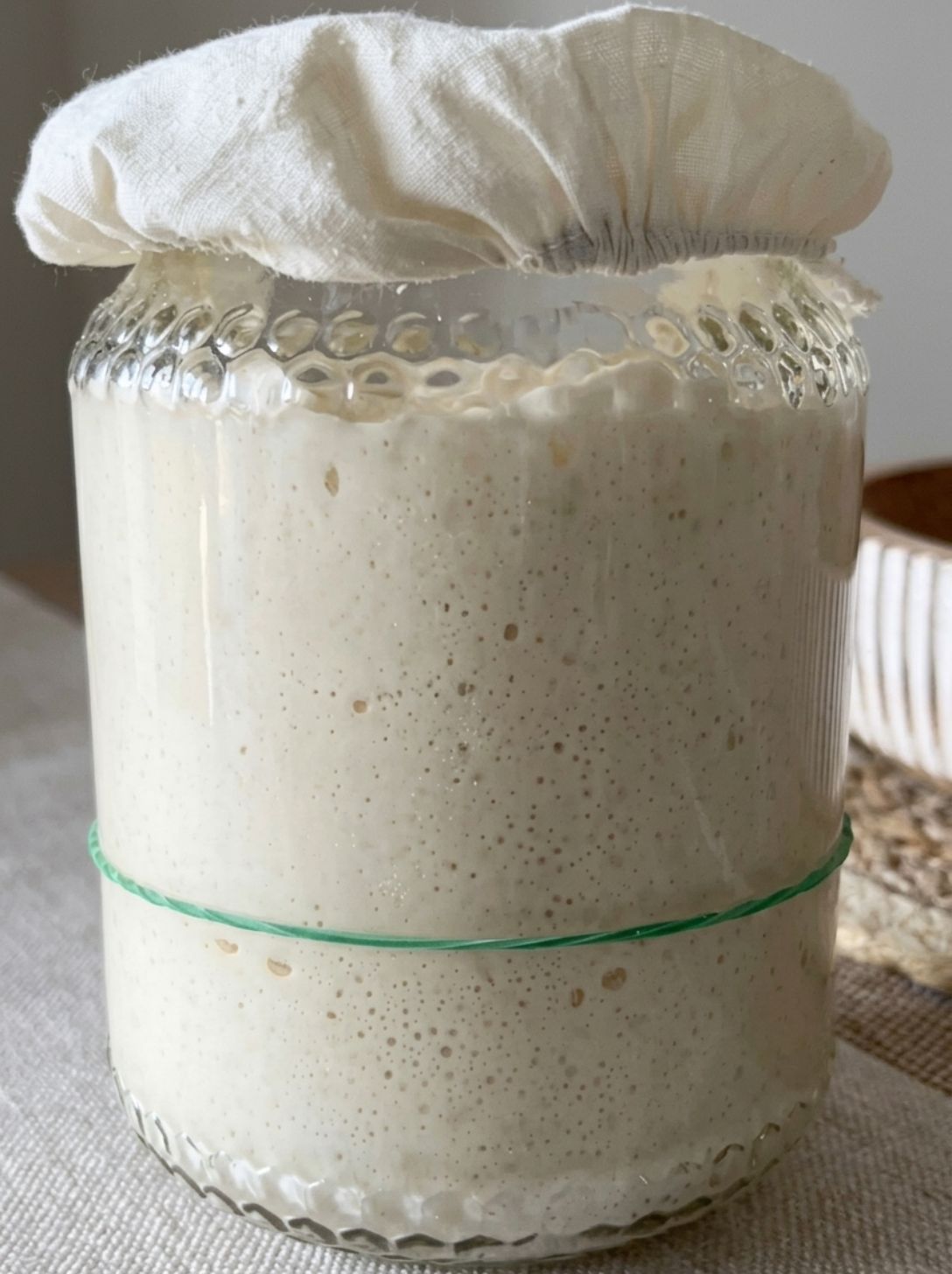 Sourdough starter risen tall in a glass jar, holding its height before collapsing