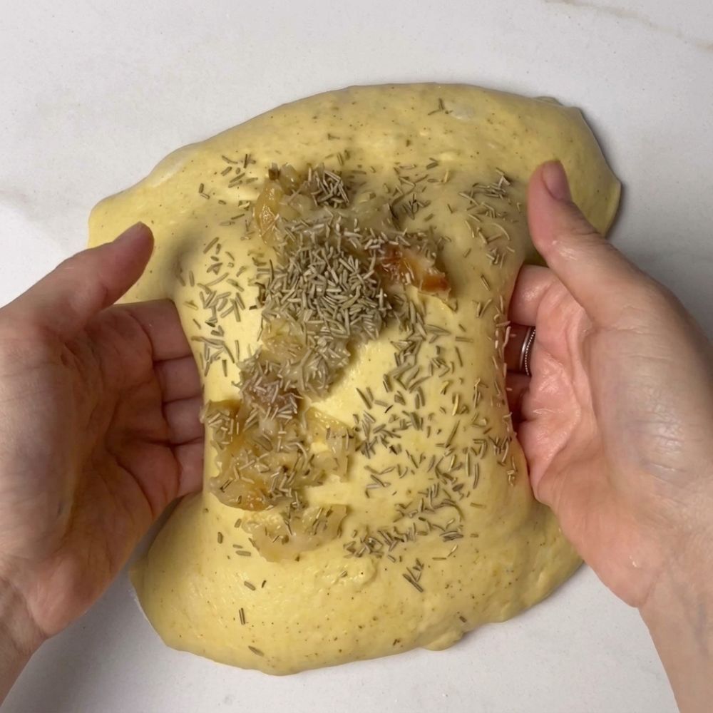 Sprinkling rosemary and oregano onto saffron sourdough dough