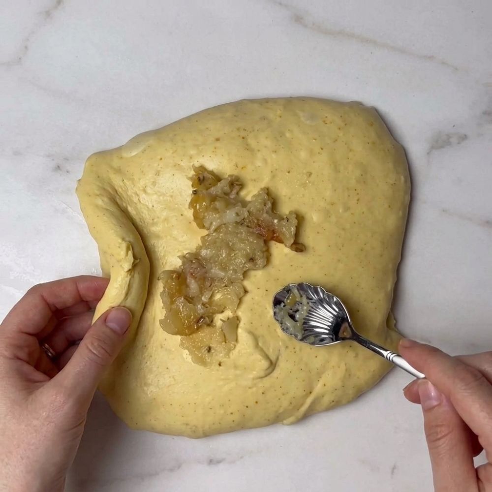 Spreading roasted garlic paste over saffron sourdough dough with a spoon
