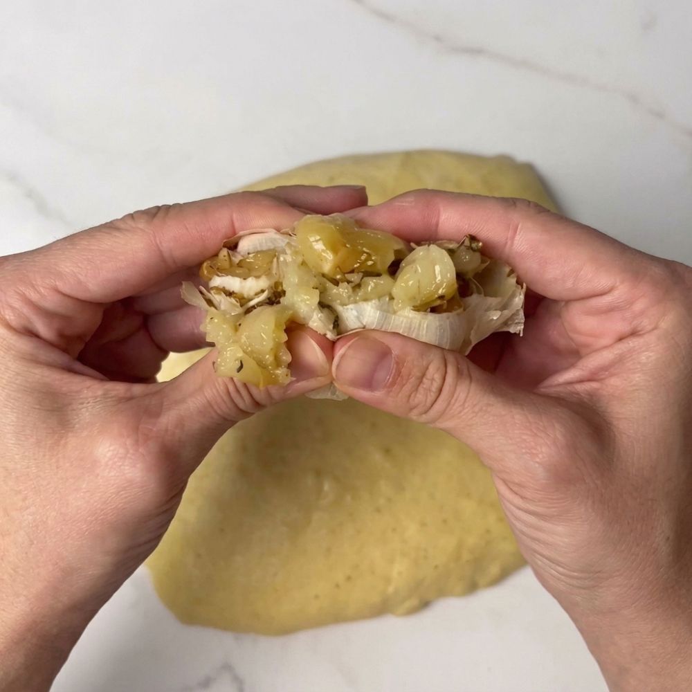 Hands squeezing roasted garlic onto saffron sourdough dough